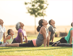 People of all ages do a yoga pose outdoors in a park.